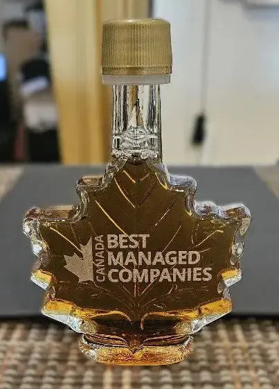 Maple syrup bottle with 'Best Managed Companies' engraving on a blurred indoor background