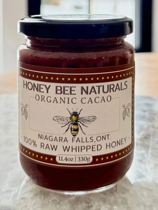 Jar of Honey Bee Naturals Organic Cacao honey on a wooden surface with a window in the background