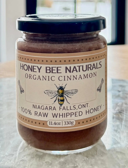 Jar of Honey Bee Naturals organic cinnamon honey on a wooden surface with a blurred background